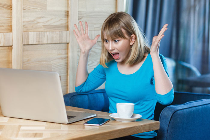 Woman in blue shirt reacting with shock while looking at laptop, illustrating venue host cleaning bill and guest reputation dispute. Woman in blue shirt reacting with shock while looking at laptop, illustrating venue host cleaning bill and guest reputation dispute.