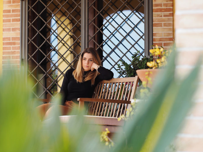 Woman sitting on wooden bench outdoors looking thoughtful with plants in foreground, representing coupon dinner debate.