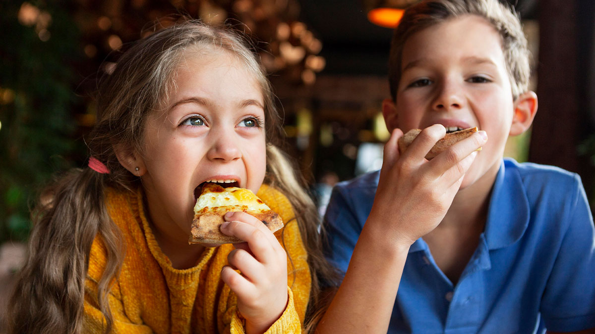 Two children enjoying pizza at dinner, illustrating a fun family moment related to saving money with a coupon.