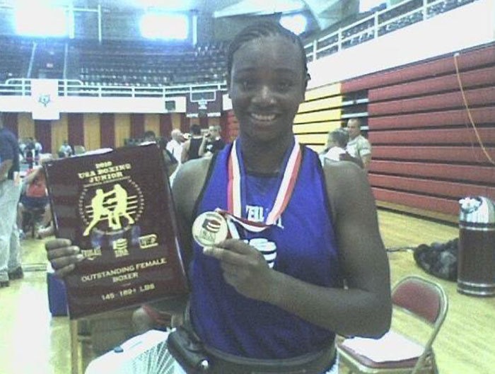 Young female boxing champ Claressa Shields holding a medal and award plaque showcasing her boxing achievements.