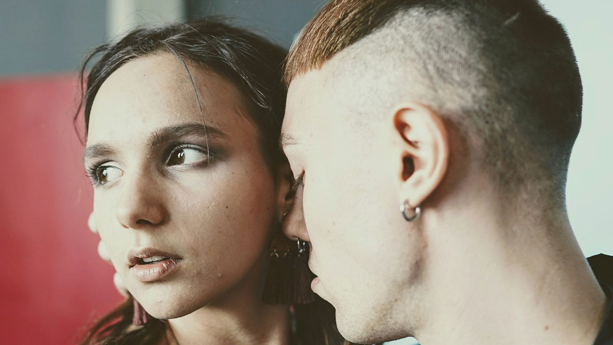 Close-up of a person whispering to a close friend who looks shocked, illustrating moments realizing a friend was a jerk.