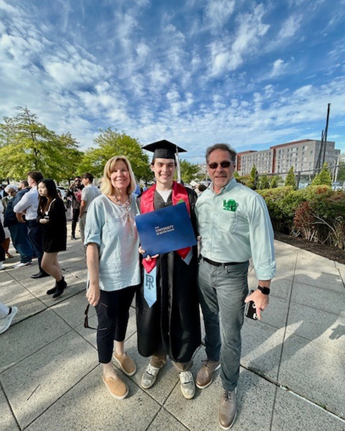 College student in graduation gown holding diploma, smiling with family outdoors on a sunny day after ceremony. College student in graduation gown holding diploma, smiling with family outdoors on a sunny day after ceremony.