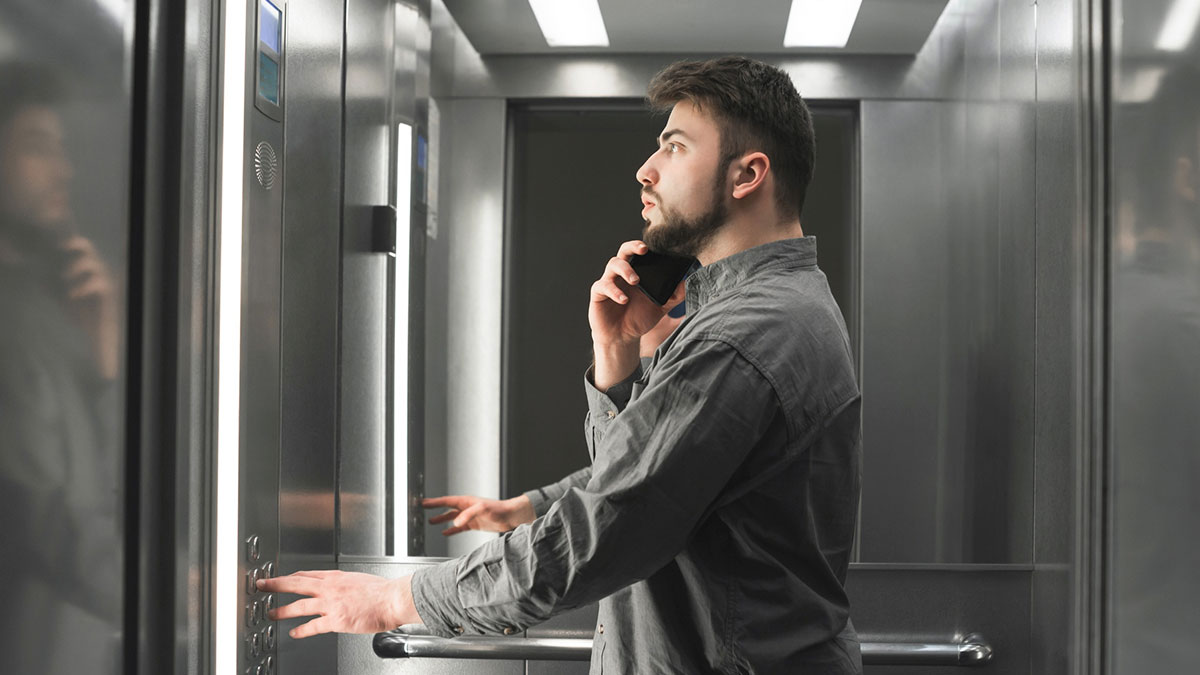Man in elevator speaking on phone, pressing buttons, exhibiting calm and composed behavior, total psychopath concept.