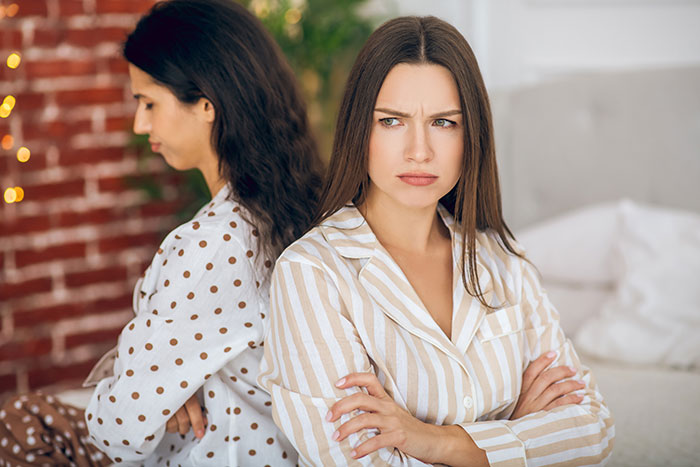 Two sisters in pajamas sitting back to back with crossed arms, showing tension in a wedding dress sisters drama. Two sisters in pajamas sitting back to back with crossed arms, showing tension in a wedding dress sisters drama.