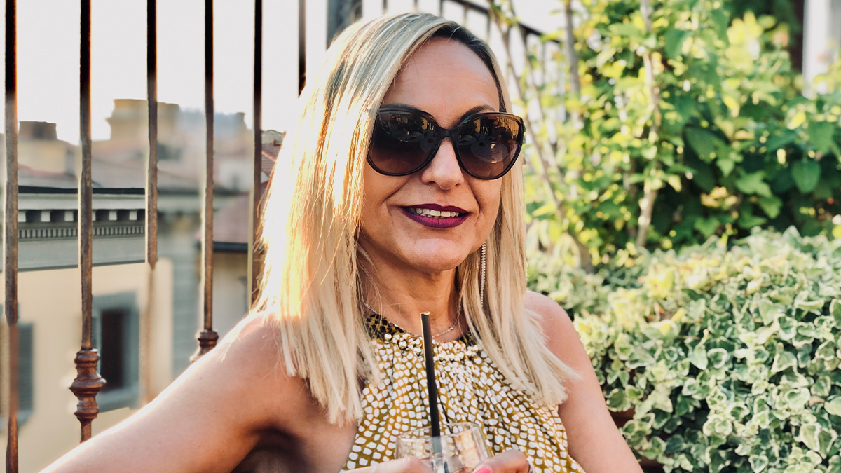 Woman with sunglasses and blonde hair smiling outdoors, representing cool kids who peaked in high school now.