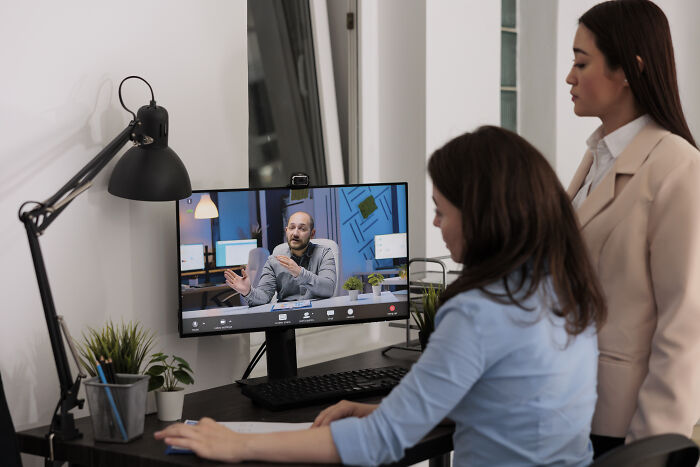 Two women watching a corporate video call on a desktop, illustrating ways to call out corporate pals’ lies professionally.