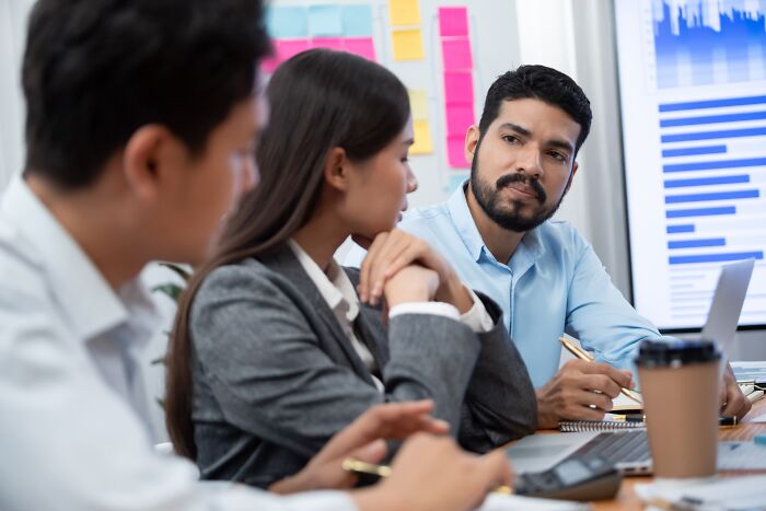 Three corporate colleagues in a meeting room, discussing and calling out lies during a serious office conversation.