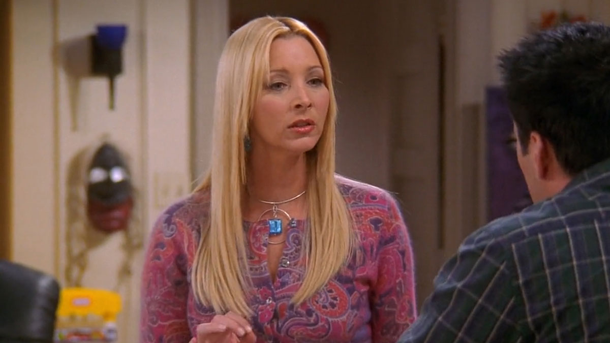 Woman dressed as Phoebe Buffay from Friends talking to a man indoors at a casual cosplay party setting.