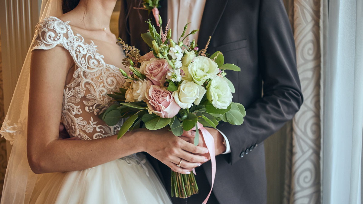 Bride in lace wedding dress holding bouquet with groom in black suit during chaotic wedding ceremony