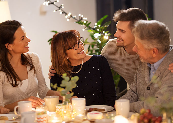 Woman smiling with family around a dinner table, discussing MIL landscaping her garden without permission after vacation. Woman smiling with family around a dinner table, discussing MIL landscaping her garden without permission after vacation.
