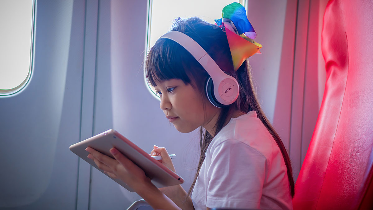 Young girl wearing headphones using tablet on an airplane, highlighting kids traveling in first class during a flight.