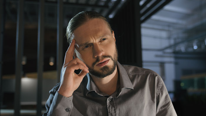 Man in gray shirt thoughtfully touching temple, reflecting on a job cousin finds through a friend conversation. Man in gray shirt thoughtfully touching temple, reflecting on a job cousin finds through a friend conversation.