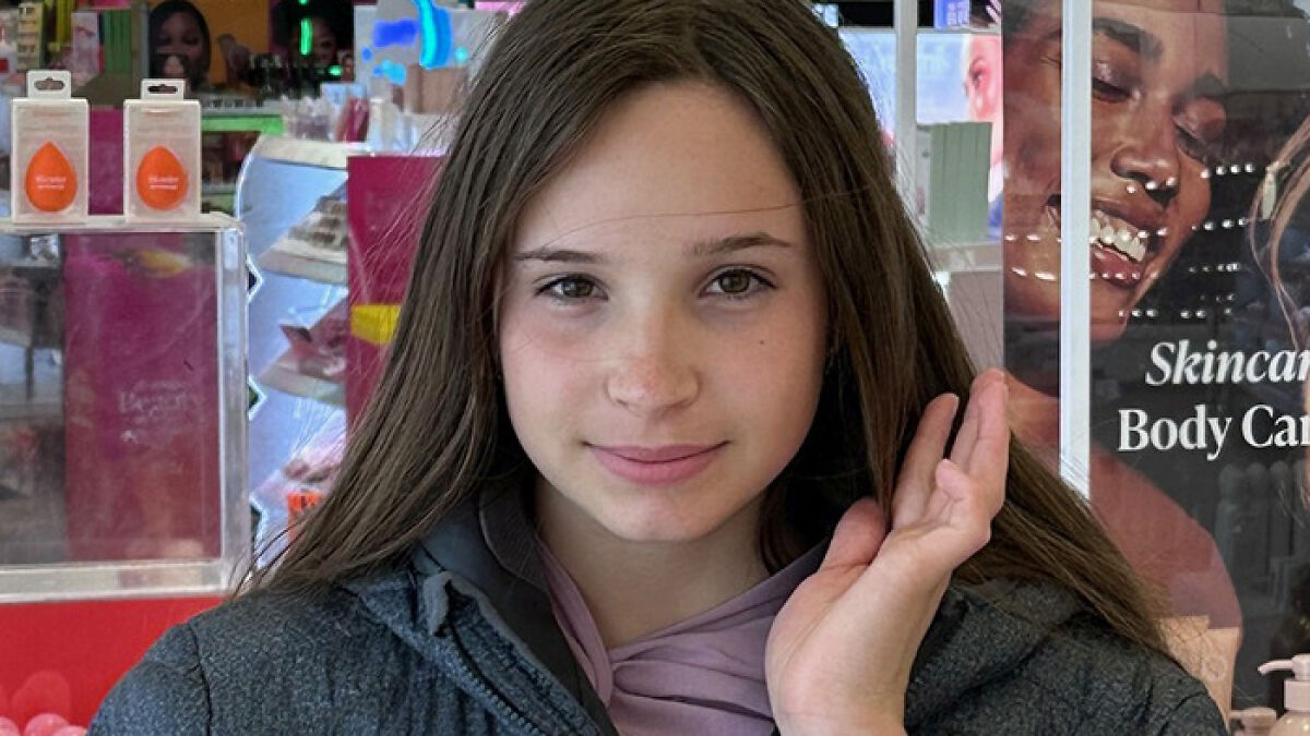 Teenage girl with long brown hair smiling softly, indoors near cosmetic displays, representing missing girl found alive.