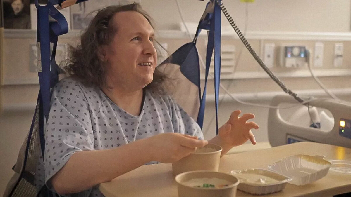 Man in hospital gown sitting in hospital bed eating food, highlighting hospital staff treatment concerns.