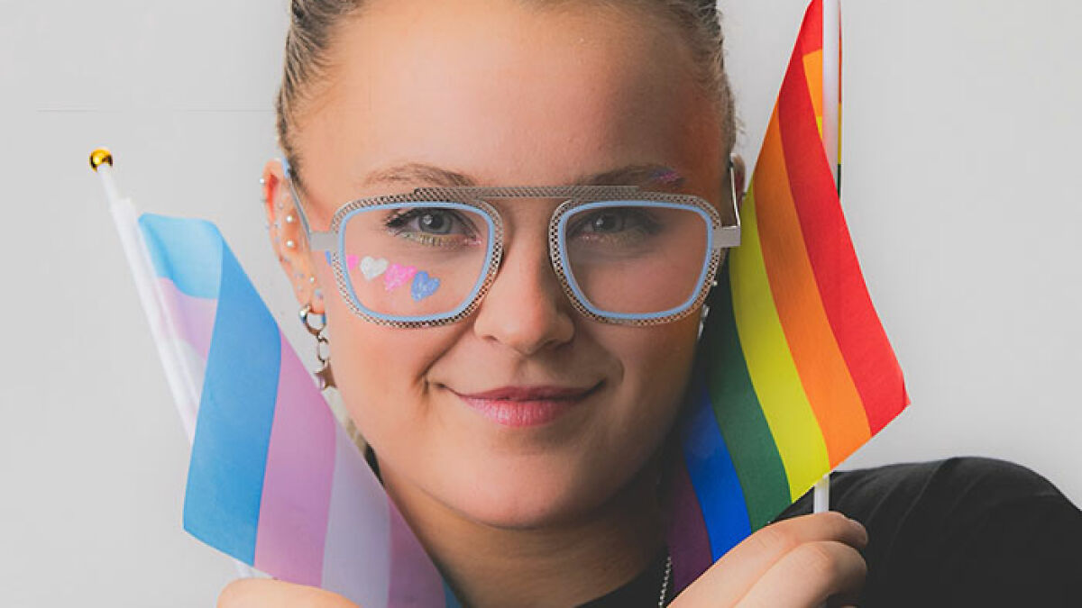 JoJo Siwa smiling with pride flags and heart stickers on cheeks, showing support for LGBTQIA+ community.