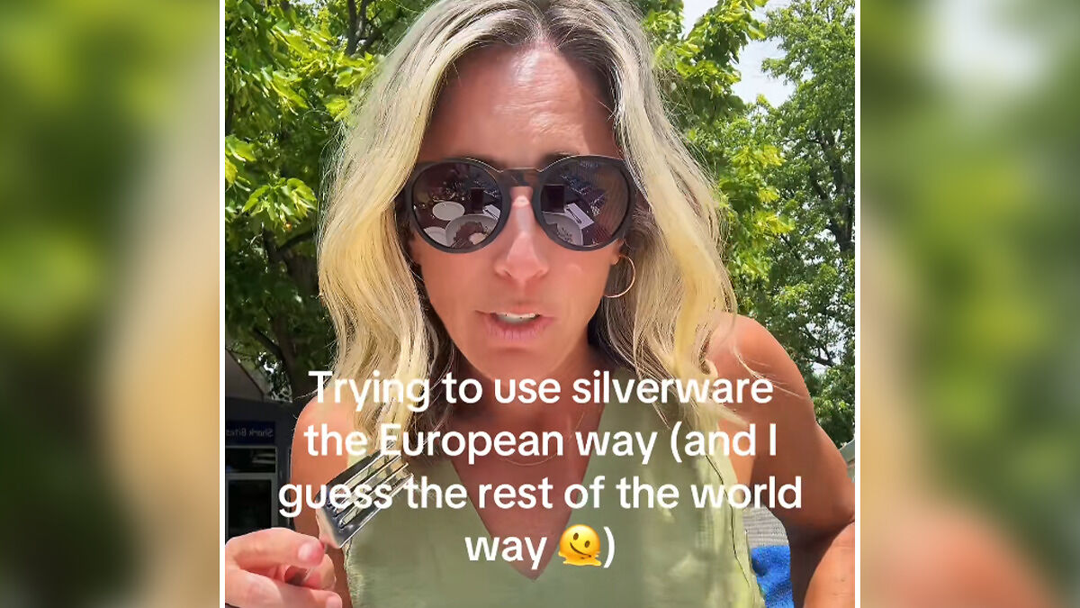 Woman outdoors wearing sunglasses, attempting to use silverware the European way, referencing primitive eating with cutlery.