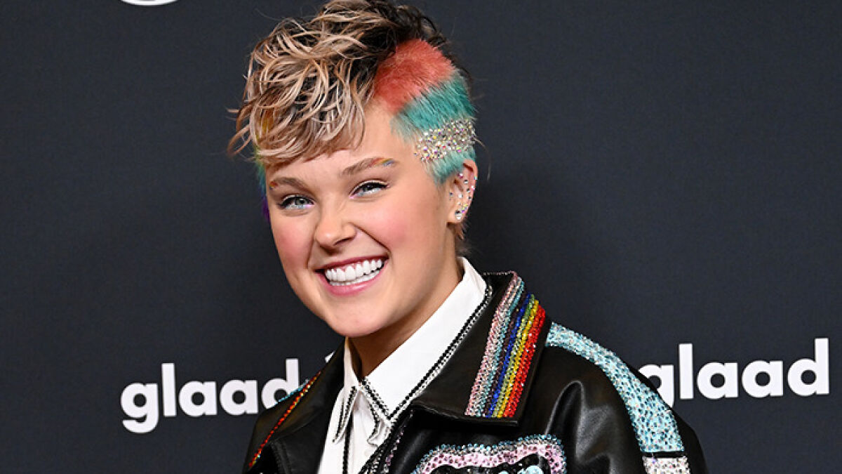 Smiling person with colorful hair and a rainbow jacket at an event, illustrating famous lesbians with boyfriends trend.