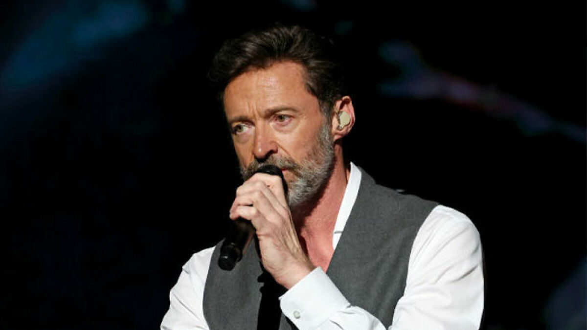 Hugh Jackman performing on stage with microphone, showing emotion amid divorce setback news.