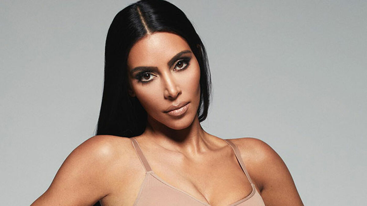 Woman with long black hair and bold makeup wearing a daring n**e bodysuit, sparking Kim K clone comments online.