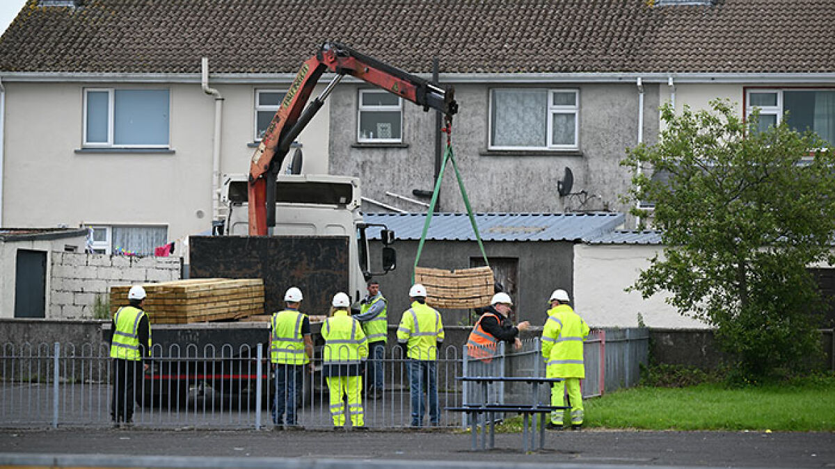Construction workers unloading wooden planks at a site linked to septic tank investigation of babies' bodies at Catholic home.