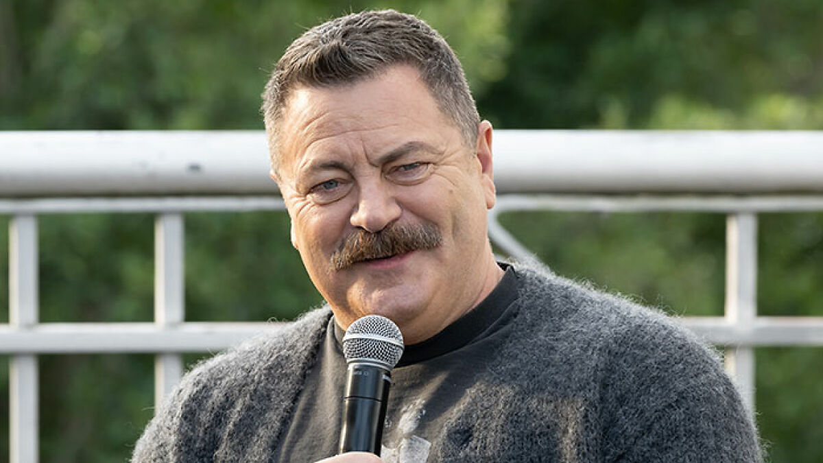 Nick Offerman speaking into a microphone outdoors, praised for a brutal clapback against homophobe in church context.