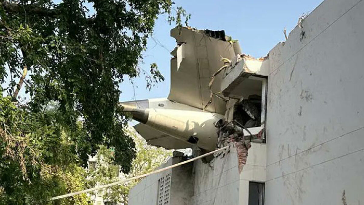 Air India survivor stands near damaged building with airplane wreckage after tragic crash, expressing survivor guilt and loss.