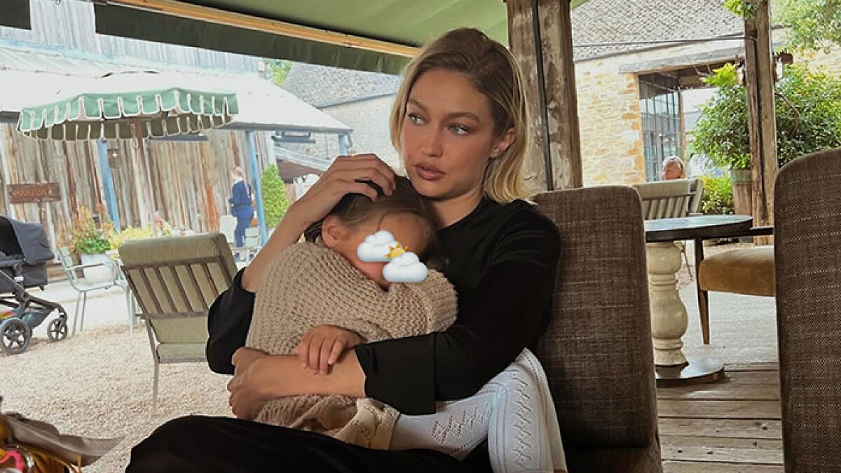 Gigi Hadid sitting outdoors holding daughter Khai, whose face is covered with weather emojis, in a cozy setting.
