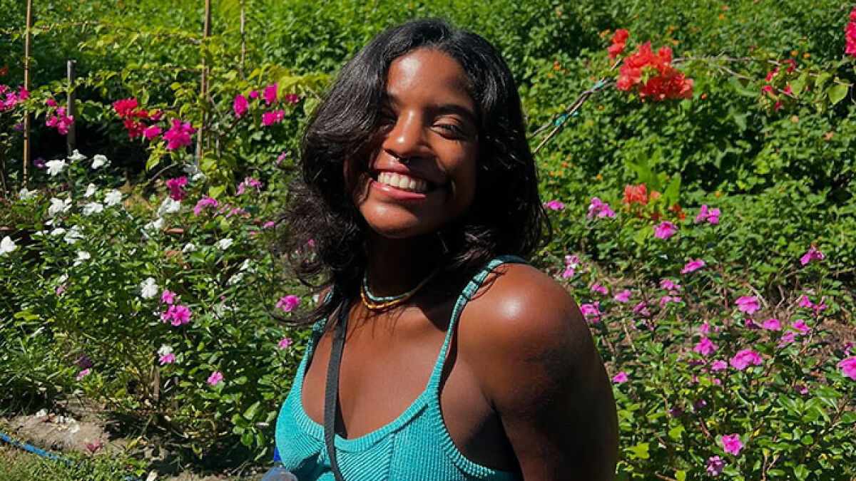 Smiling female tourist in blue top surrounded by flowers, linked to abandoned hike incident on Indonesian volcano.