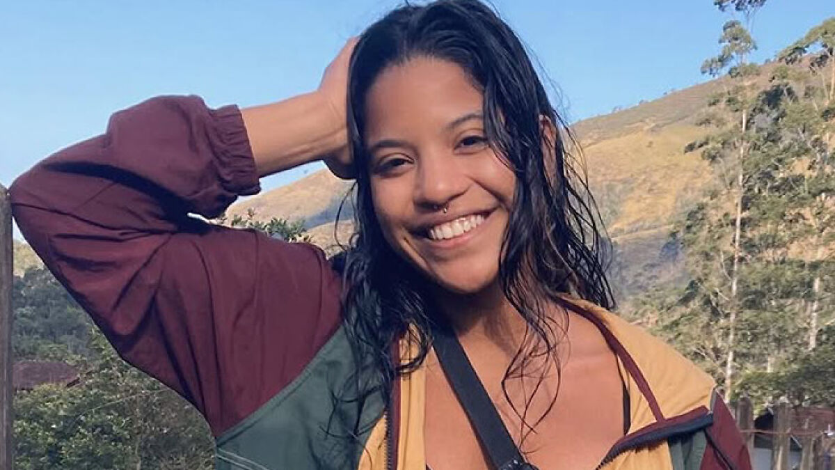 Young tourist smiling outdoors with wet hair and casual jacket, amid growing outrage over active volcano abandonment.