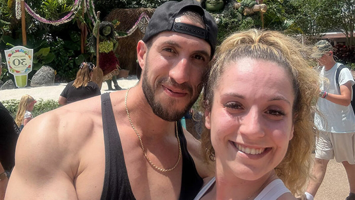 Smiling woman and man at Disney park, woman involved in debate over Disney staff scolding her outfit as inappropriate.