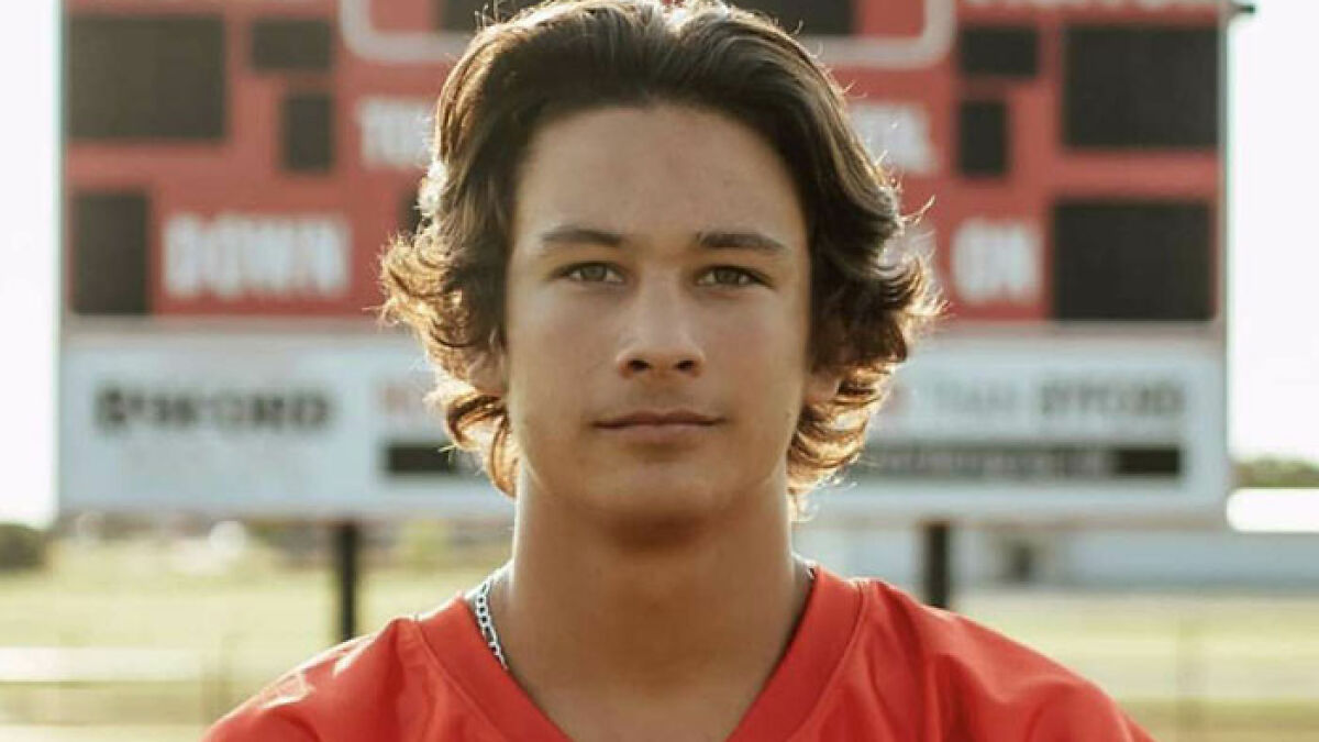 Teen standing in red sports jersey with scoreboard in background, related to lawsuit and named suspects case.