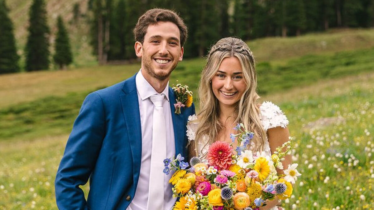 Newlyweds smiling in wedding attire outdoors with colorful bouquet, moments before honeymoon tragedy in ankle-deep water.
