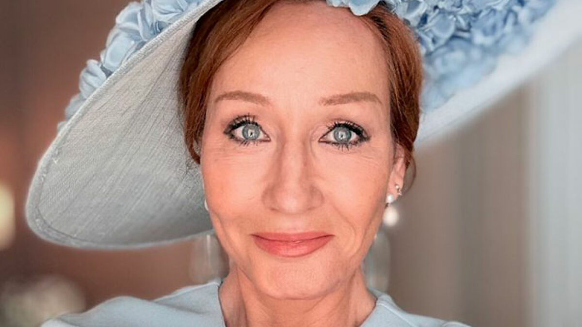 Close-up portrait of JK Rowling wearing a light blue hat and matching outfit with pearl earrings in soft lighting.