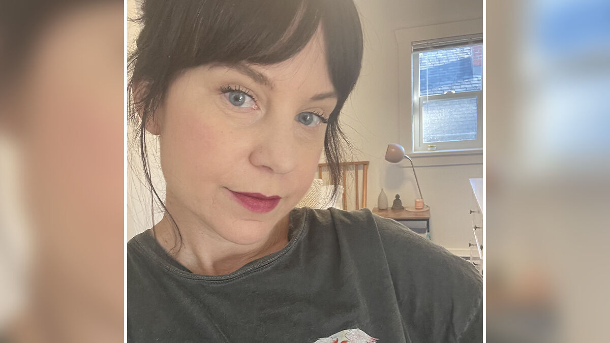Single mom with early-onset Alzheimer's wearing dark shirt, looking contemplative in a softly lit bedroom setting.