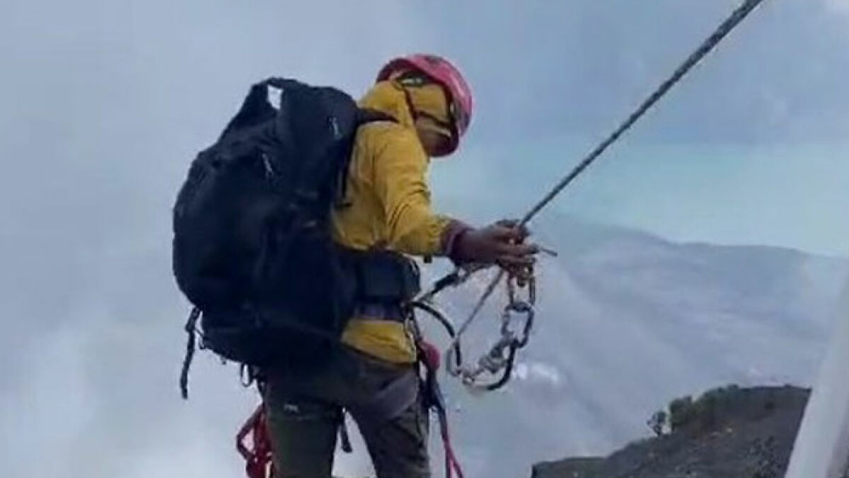 Guide climbing an active volcano using safety ropes during recovery of tourist's body from deep crater.