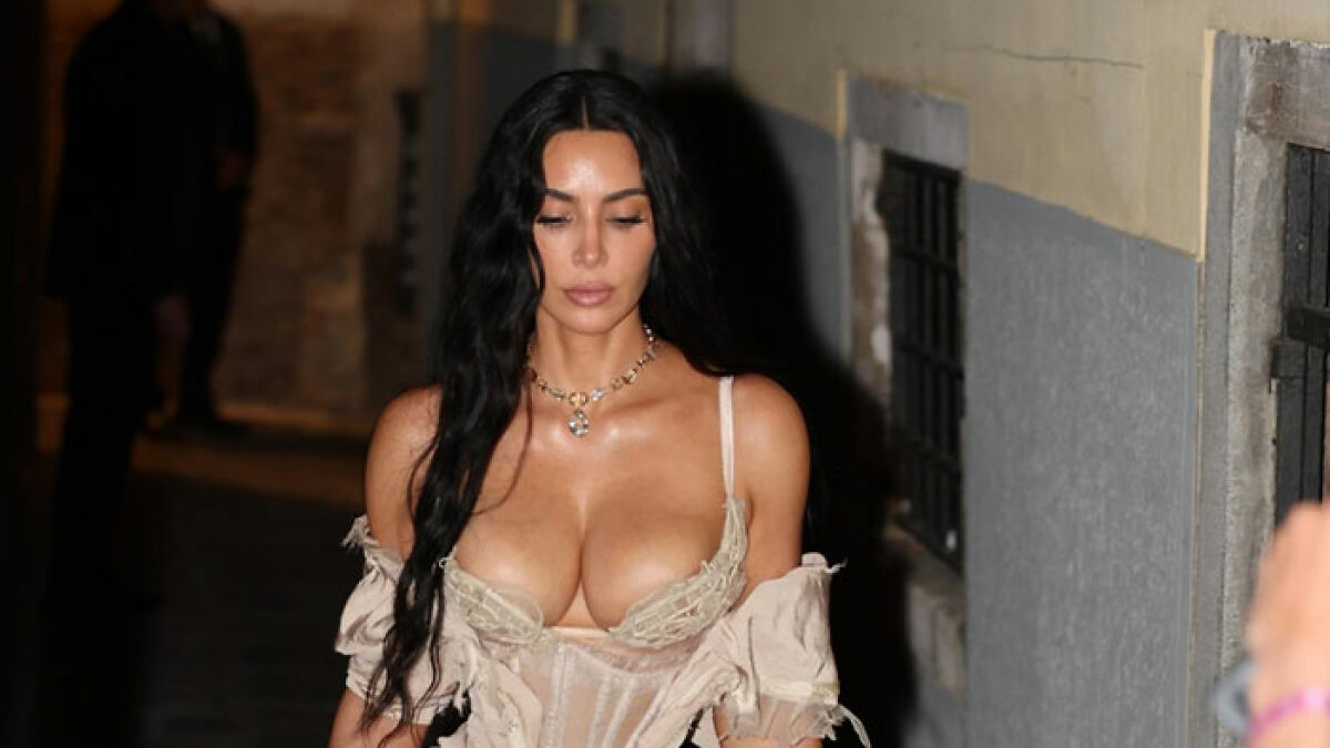 Kim Kardashian in beige lingerie walking outdoors at night, showcasing a stunning and bold fashion statement.