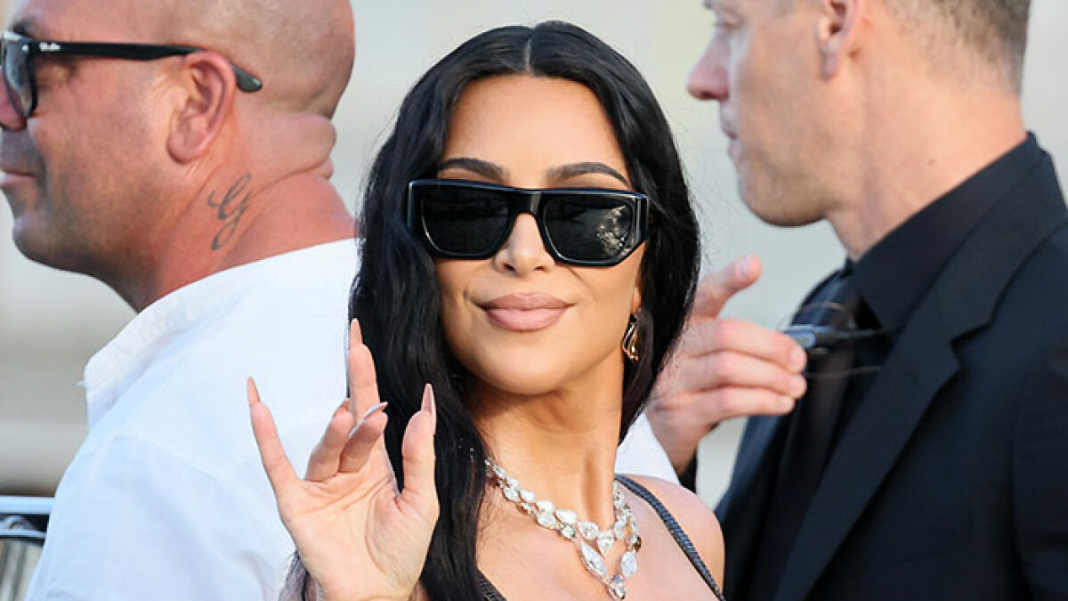 Kim Kardashian wearing sunglasses and jewelry, smiling and waving, related to Jeff Bezos wedding ceremony reactions.