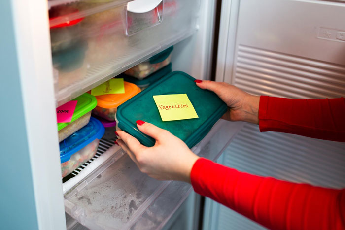 Hands placing a labeled food container inside a fridge as workers add labels to protect their food from lunch thieves.