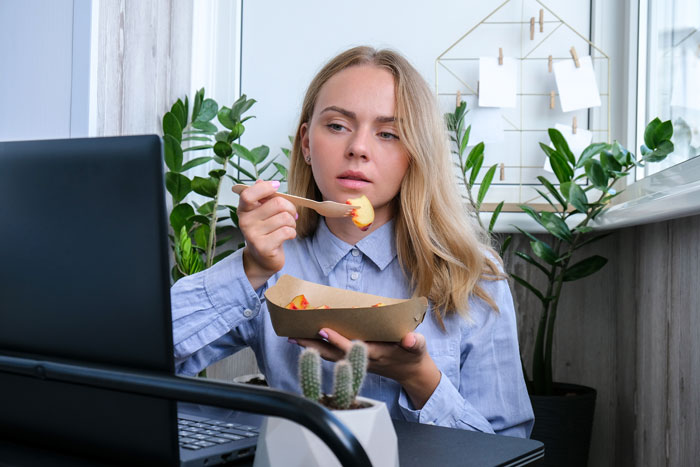 Woman eating lunch at her desk, illustrating workers adding labels to protect food from lunch thieves. Woman eating lunch at her desk, illustrating workers adding labels to protect food from lunch thieves.