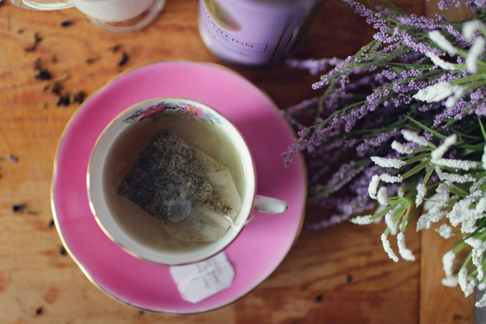 Tea bag steeping in a floral cup on a pink saucer next to lavender flowers, hinting at a coworker tea thief at work. Tea bag steeping in a floral cup on a pink saucer next to lavender flowers, hinting at a coworker tea thief at work.