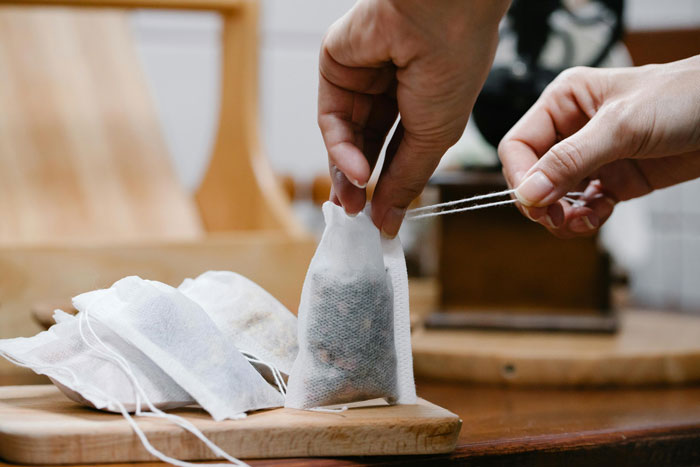 Hands holding a tea bag with other tea bags on a wooden surface, illustrating a coworker tea thief at work. Hands holding a tea bag with other tea bags on a wooden surface, illustrating a coworker tea thief at work.