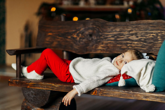 Child lying on wooden bench indoors, wearing warm clothes, depicting a cold night and troubled family situation.