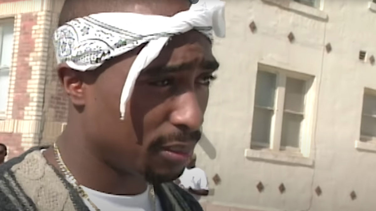 Close-up of a celebrity with a white bandana discussing the wildest rumors going around in a sunny outdoor setting.