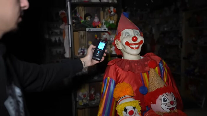 Person using device near creepy clown dolls in dark room, illustrating creepy and chilling spots in the U.S.