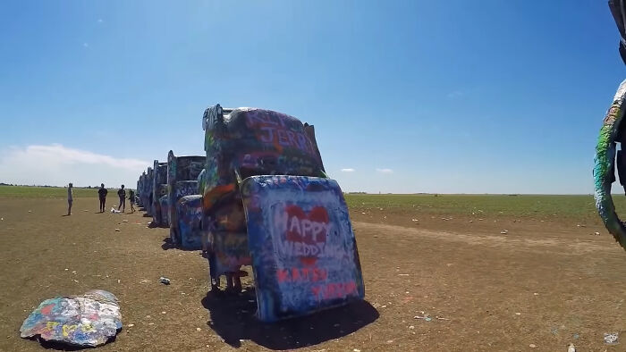 Creepy and chilling spots in the U.S. featuring graffiti-covered cars buried in the ground under a clear blue sky.
