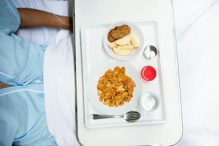 Hospital patient meal tray with pasta, apple slices, cookies, and drinks, illustrating coworker diabolical things to report HR.