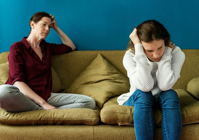 Two women on a couch showing subtle signs of incredibly low self-esteem in an emotional moment at home.