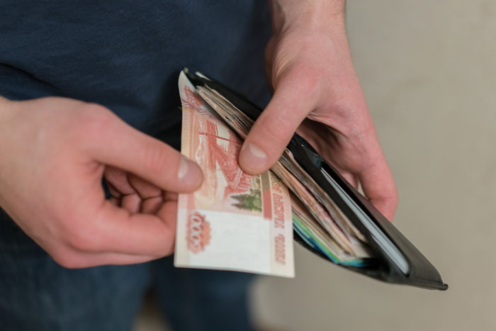 Man holding wallet with cash, relating to woman telling guy no spark after first date and payment demand.