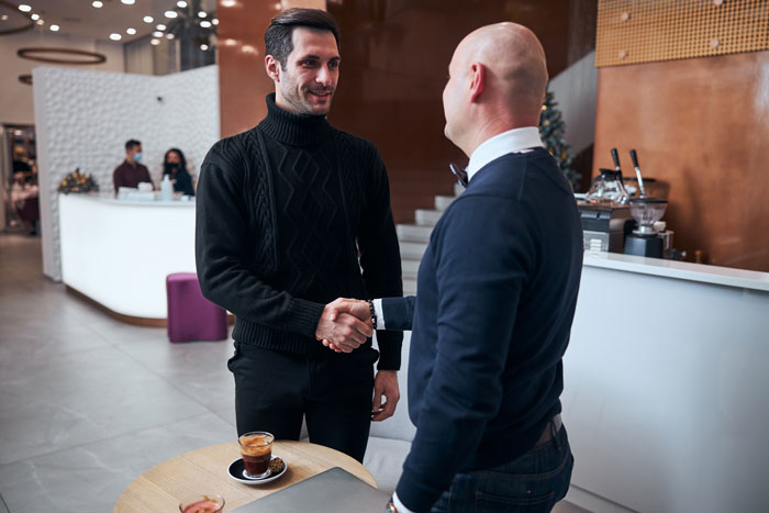 Two men shaking hands at a cafe table with coffee, illustrating a tense first date interaction without a romantic spark.