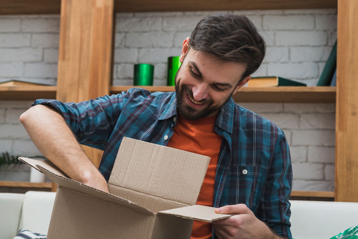 Man smiling while unpacking a cardboard box at home, representing a first date interaction with no spark and meal payment issue.